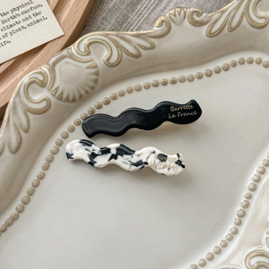 Detail of wavy acetate hair clips in black and marble patterns on a ceramic tray