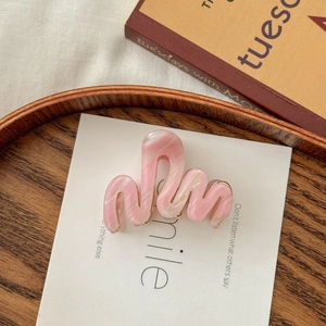 Détail d'une pince à cheveux vague en marbre rose sur assiette en bois avec livre