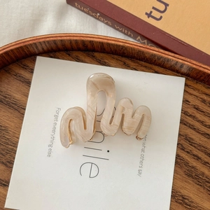 Détail d'une pince à cheveux vague à texture marbrée beige sur une carte d'affichage
