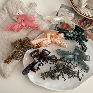 Elegant acetate bow hair claws in multiple colors arranged on a white ceramic plate