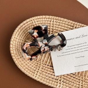 Detailed view of tortoiseshell acetate bow hair claw clip with rhinestones and metal logo