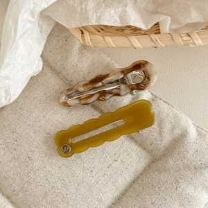 Détail de barrettes à cheveux ondulées en acétate sur un support en lin naturel
