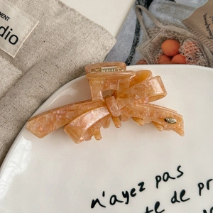 Detailed macro view of orange-pink marble acetate bow hair claw clip with gold metal logo