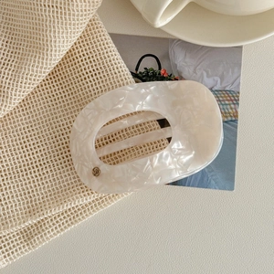 Détail d'une pince à cheveux vintage en acétate marbré crème avec un petit logo en métal