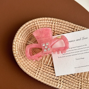 Detail view of pink acetate hair claw with sparkling rhinestones on a woven mat