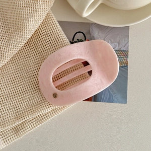 Détail d'une pince à cheveux en acétate marbré rose avec logo MY doré sur un sac neutre