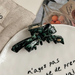 Detail view of dark green marble acetate hair claw clip with golden logo emblem and spring