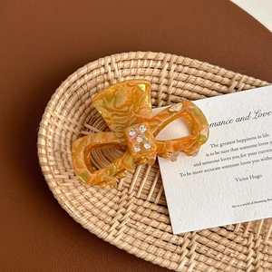 Detail shot of orange marble pattern acetate hair claw with sparkling rhinestone bow inlay