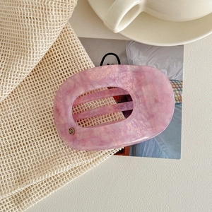 Détail d'une pince à cheveux en acétate rose marbré avec ornement doré sur tissu