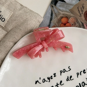 Pink marble acetate bow hair claw clip with gold logo on a French style white plate