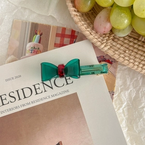 Détail de la pince à cheveux en acétate vert et rouge posée sur un magazine avec raisins