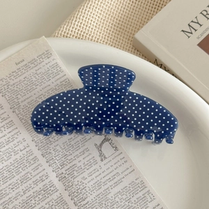 Detail of navy blue polka dot hair claw clip on white ceramic plate with vintage paper