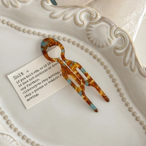 Detail of a handmade tortoise shell hair fork with blue accents on a vintage porcelain plate