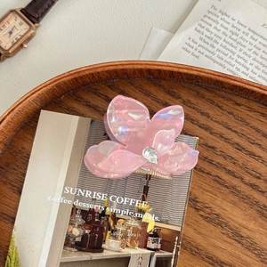 Détail d'une pince à cheveux fleur rose en acétate avec cristal sur plateau en bois