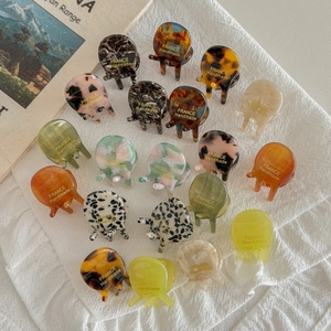 Mini acetate hair claws in tortoise and marble patterns on white linen background