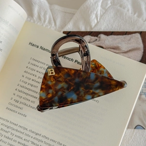 Détail d'une pince à cheveux triangle en écaille avec lettre B dorée sur un livre
