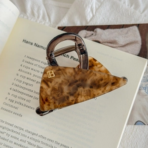 Détail de la pince à cheveux léopard en acétate avec logo B doré sur un livre
