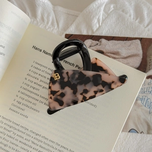 Gros plan sur pince à cheveux léopard avec lettre B dorée sur fond de livre vintage