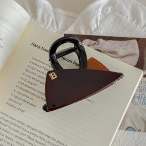 Gros plan d'une pince à cheveux ambre avec logo B doré sur un livre de cuisine