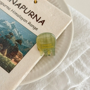 Macro shot of green mini acetate hair claw clip with gold handmade text on fabric