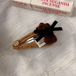 Détail d'une pince à cheveux ours en tricot marron avec nœud en velours et bouton en bois