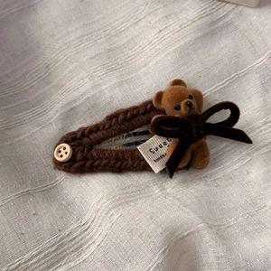 Détail d'une pince à cheveux tricotée avec ours brun, nœud en velours et bouton en bois