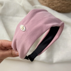 Dettaglio del cerchietto imbottito rosa con emblema di cavallo dorato tenuto in mano