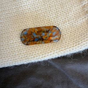 Close-up of oval amber and blue tortoise hair clip with Creation France logo text