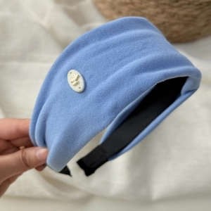 Dettaglio di cerchietto in velluto azzurro con emblema dorato e design imbottito