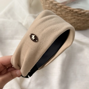 Dettaglio del cerchietto imbottito beige con emblema dorato e morbida trama in velluto