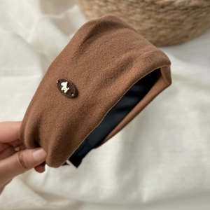 Dettaglio di un cerchietto di peluche marrone con decorazione a cane dorato e texture