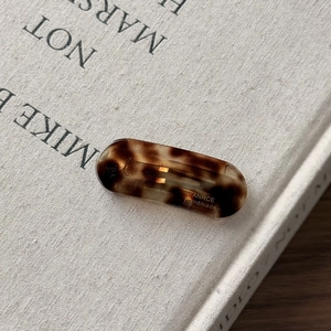 Detail view of oval tortoiseshell resin hair clip with gold metal clip on white book