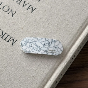Macro detail of oval acetate hair clip with grey marble texture and gold handmade logo