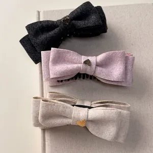 Three elegant bow hair clips with gold heart accents in black, pink, and beige colors