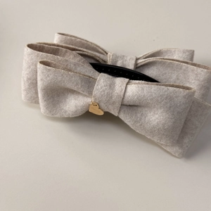 Detail of beige velvet bow hair clip with a gold heart pendant and black banana claw grip