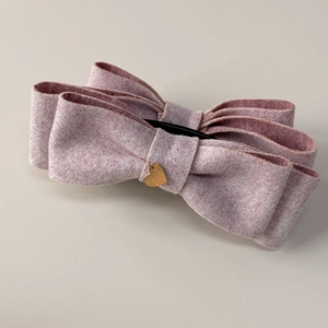 Detail of pink tweed bow hair clip featuring a layered design and gold heart charm