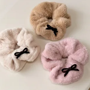 Three plush hair scrunchies in khaki, beige, and pink with small black velvet bows