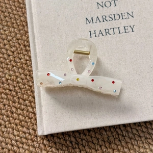 Close-up of a cream bow hair claw clip with colorful rhinestones on a textured book