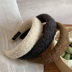 Detail of three fuzzy lamb wool headbands in beige grey and brown on white fabric