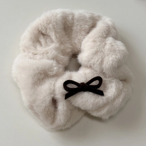 Detail of plush beige scrunchie featuring a soft faux fur texture and a brown velvet bow