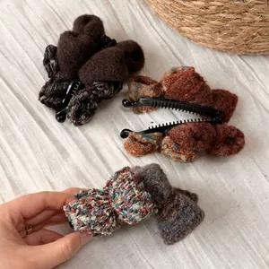 Trois pinces à cheveux à nœuds en peluche tricotée en café, orange et bleu sur tissu