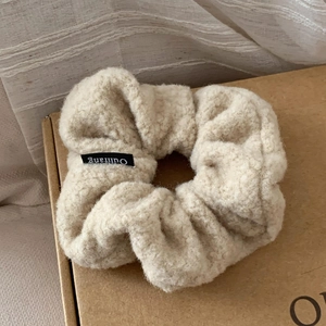 Detail of soft beige lamb wool scrunchie featuring a designer label on warm paper box