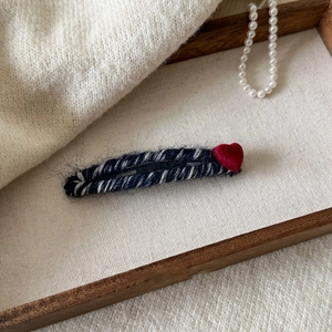 Détail d'une pince à cheveux tricotée à rayures avec un cœur rouge 3D sur plateau bois