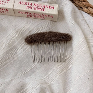 Detail of plush dark brown wool felt oval top and polished silver metal hair comb tines
