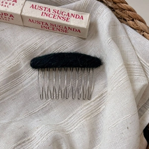 Close-up of a 10-tooth metal hair comb with black plush wool top on linen background