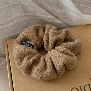 Close-up of soft camel-colored faux shearling scrunchie with brand tag on paper box