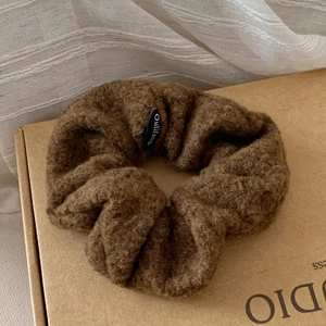 Close-up of soft brown lamb wool hair scrunchie with detailed plush texture and black label