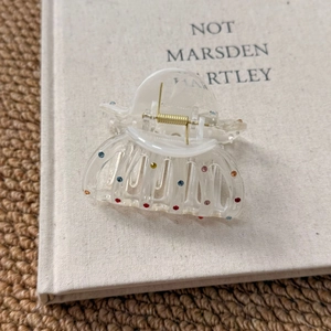 Close-up of clear acrylic star hair claw clip with colorful rhinestones on a book
