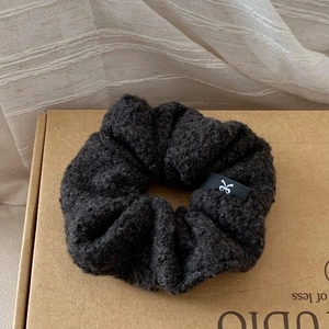 Close-up of dark grey fuzzy fleece scrunchie featuring a white bow logo tag detail