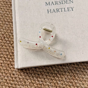 Detail of transparent acrylic hair claw clip featuring colorful rhinestones and gold spring